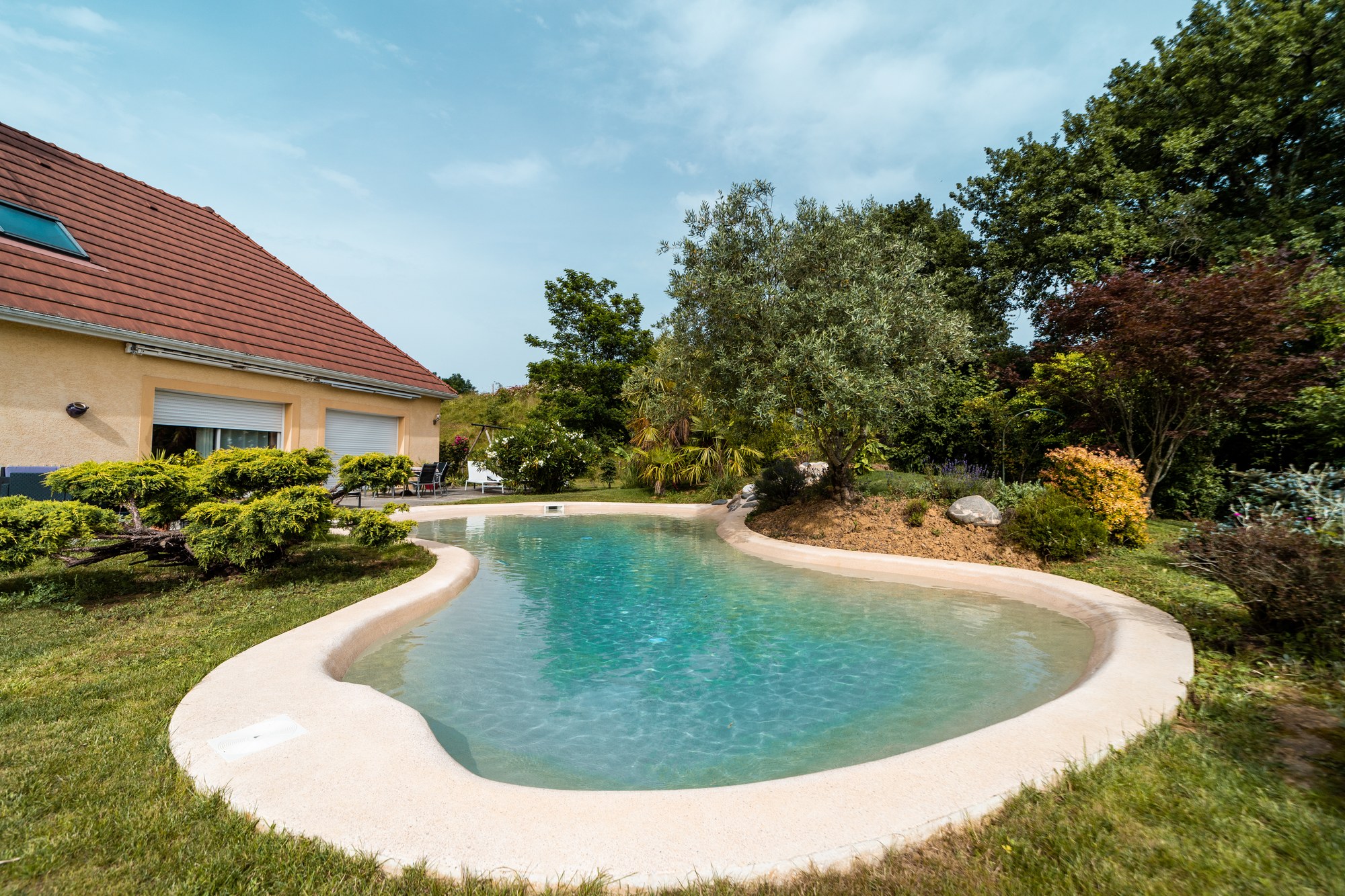 Bassin lagon de baignade éco-conçu en béton de pierre reconstituée minérale avec plages immergées en pente douce intégrale, réalisé par NaturaSwim en milieu paysager