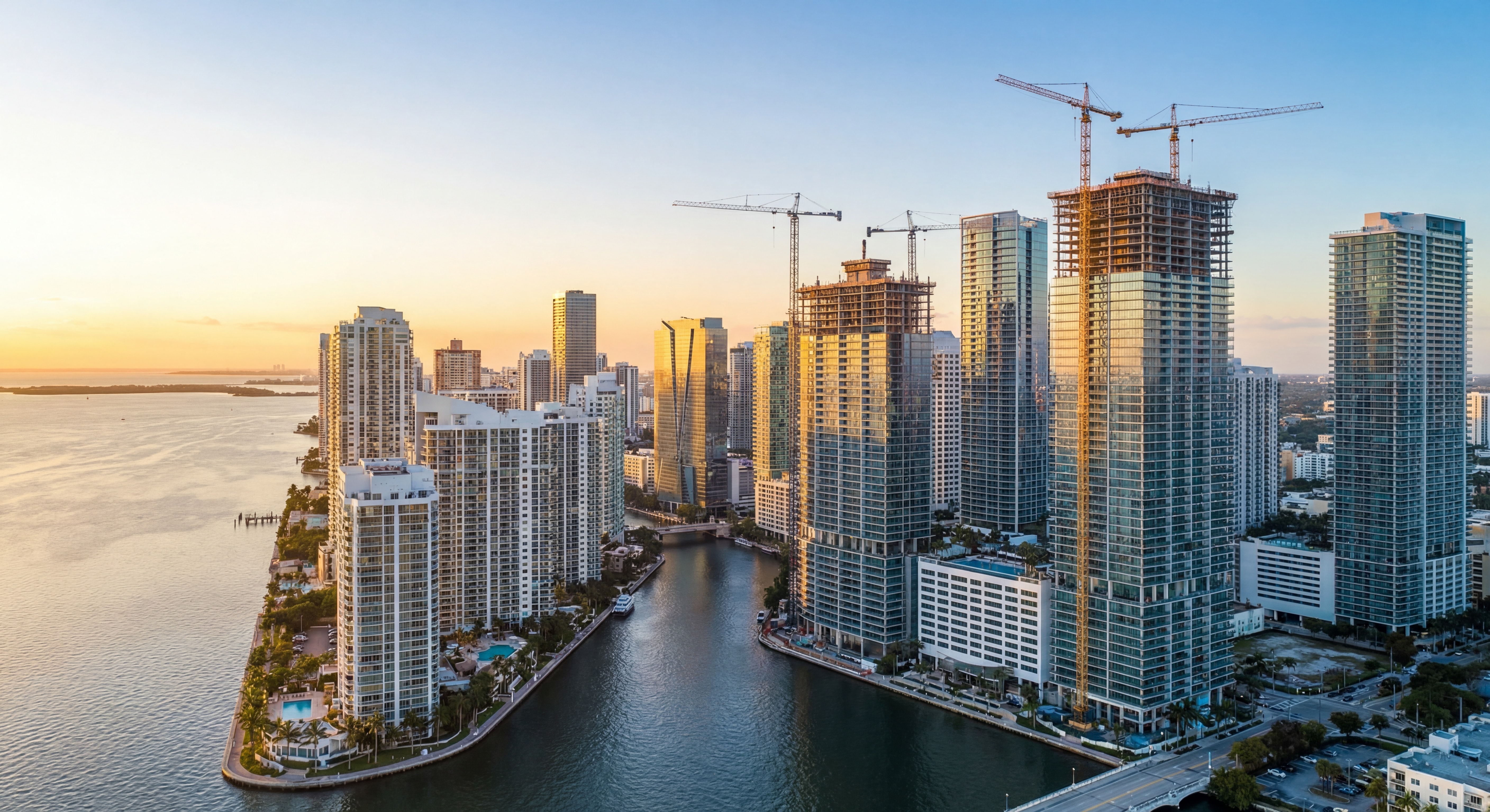 Aerial view of Miami's Brickell skyline with new luxury high-rise construction cranes at sunset, showcasing waterfront development