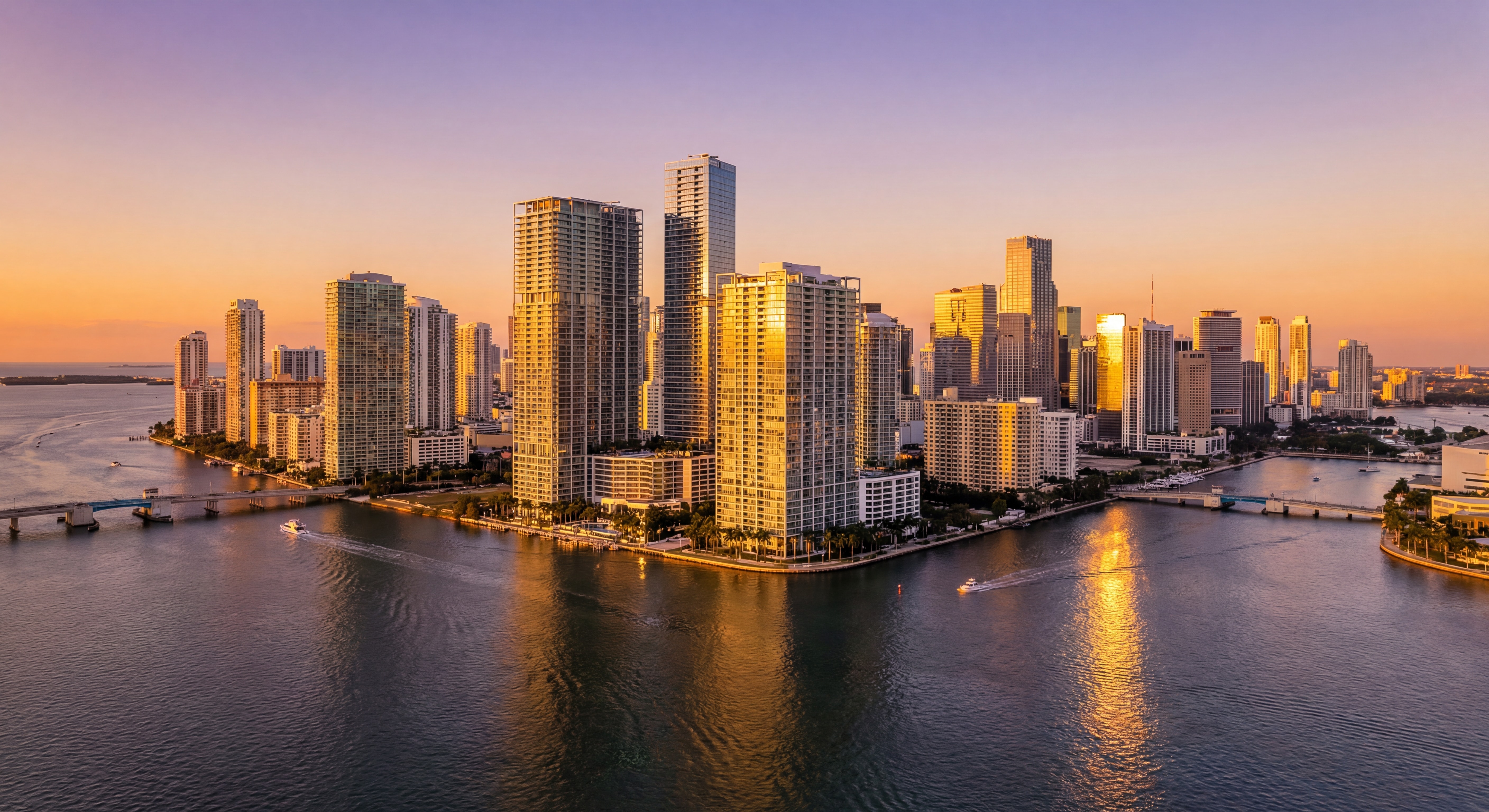 Aerial drone view of Miami's Brickell skyline at sunset with Biscayne Bay waterfront luxury towers reflecting golden light