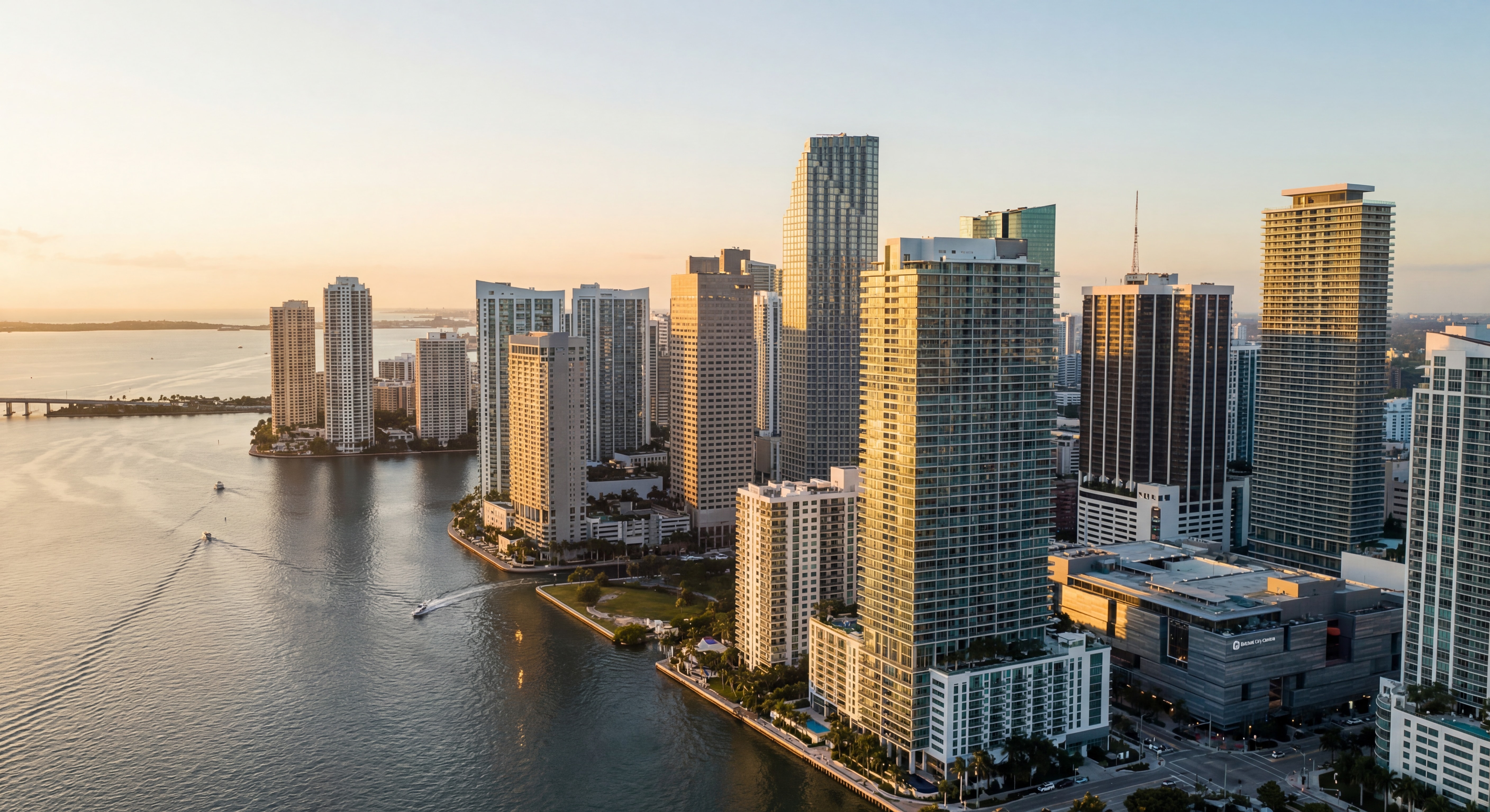 Aerial drone view of Miami's Brickell skyline at sunset with luxury high-rise condos and Biscayne Bay waterfront reflecting golden light