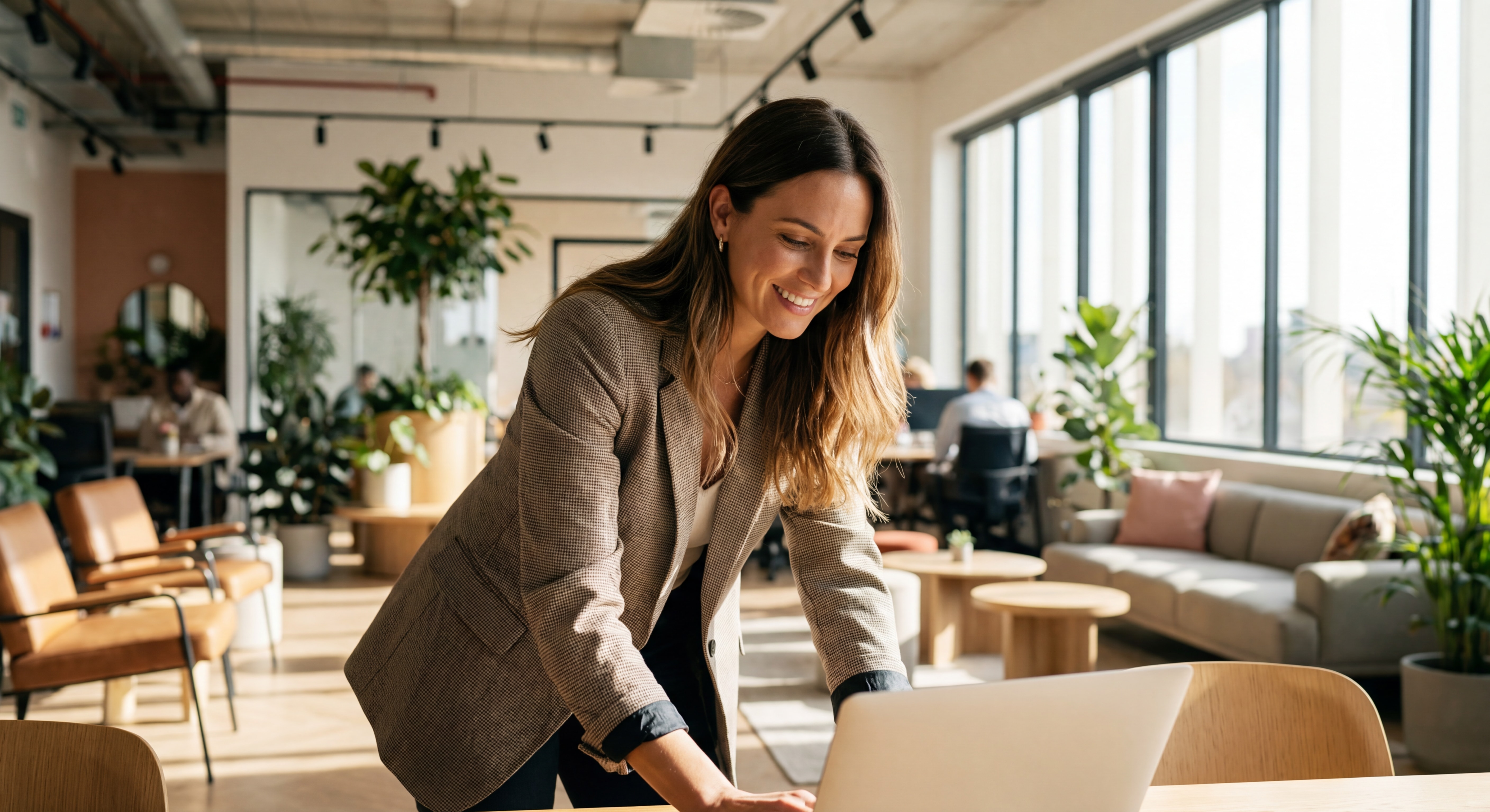 Indépendant(e) confiant(e) souriant(e) devant un laptop dans un espace de coworking moderne, lumière naturelle, posture dynamique et inspirante