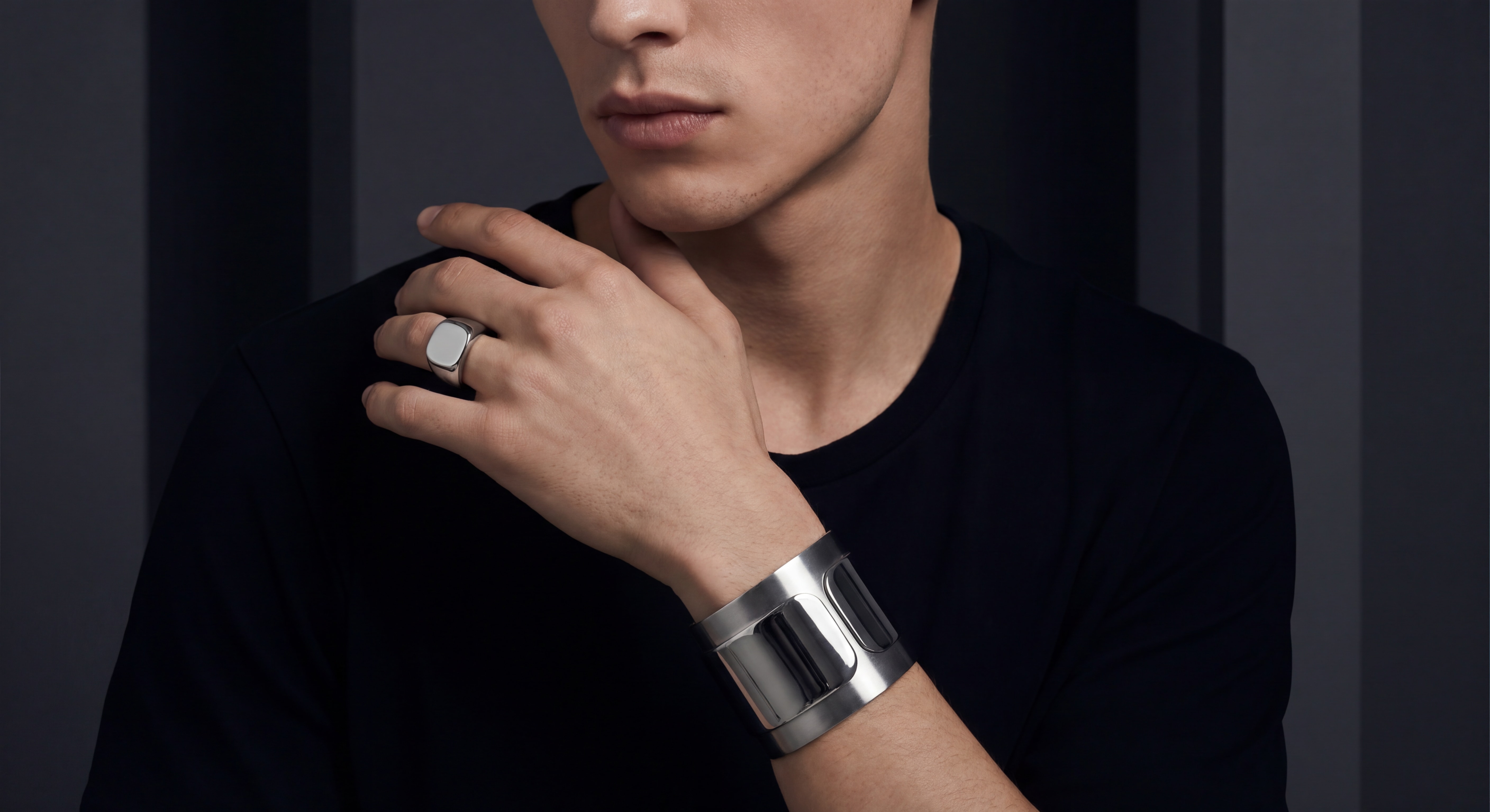 Ambiance éditoriale mode — bijoux en acier inoxydable portés dans un contexte fashion stylisé, chevalière mixte et bracelet manchette mis en valeur sur fond sombre dramatique, éclairage studio