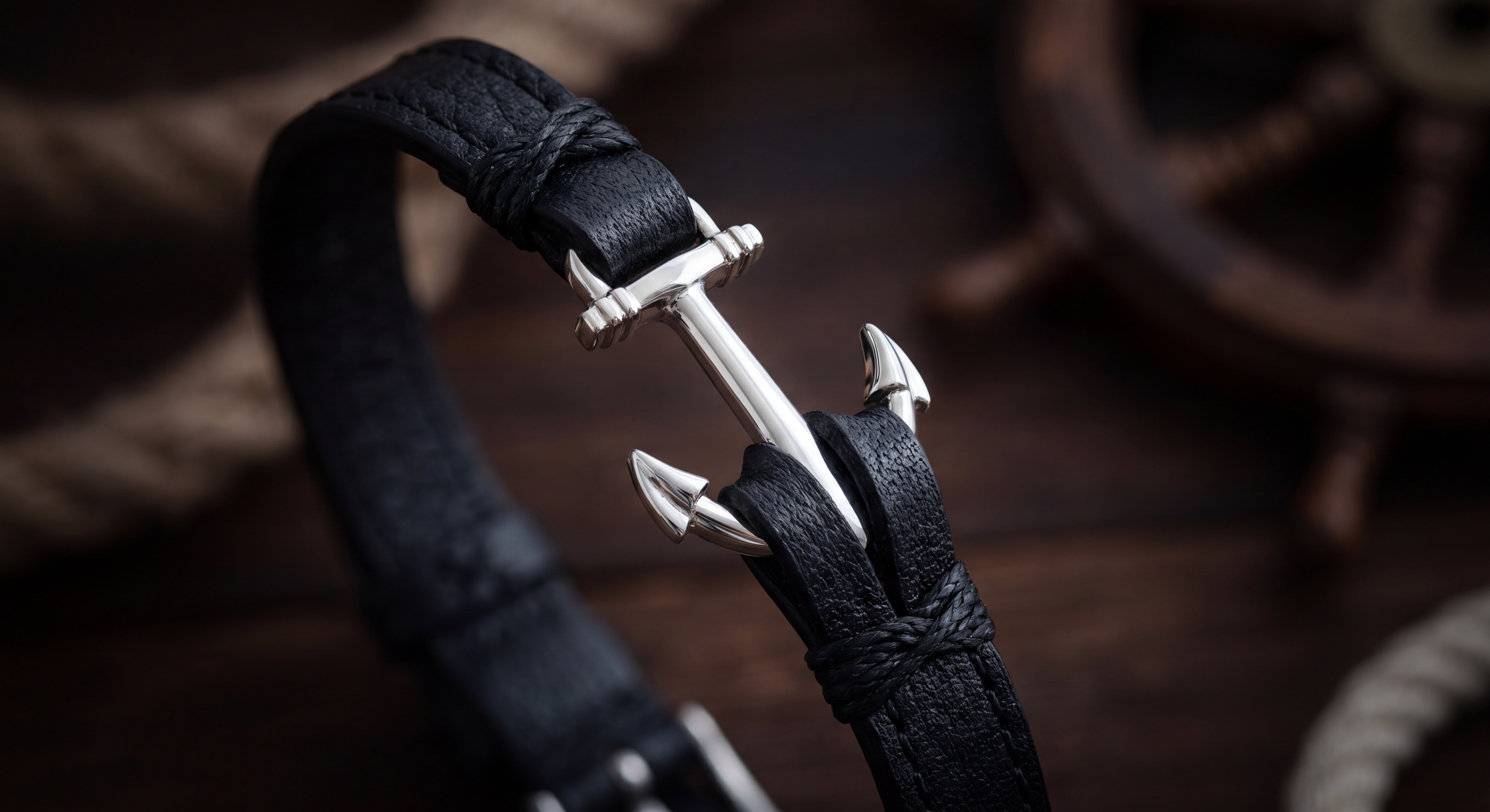 Gros plan sur le détail de l'ancre argentée sur cuir noir d'un bracelet homme nautique, fond sombre élégant