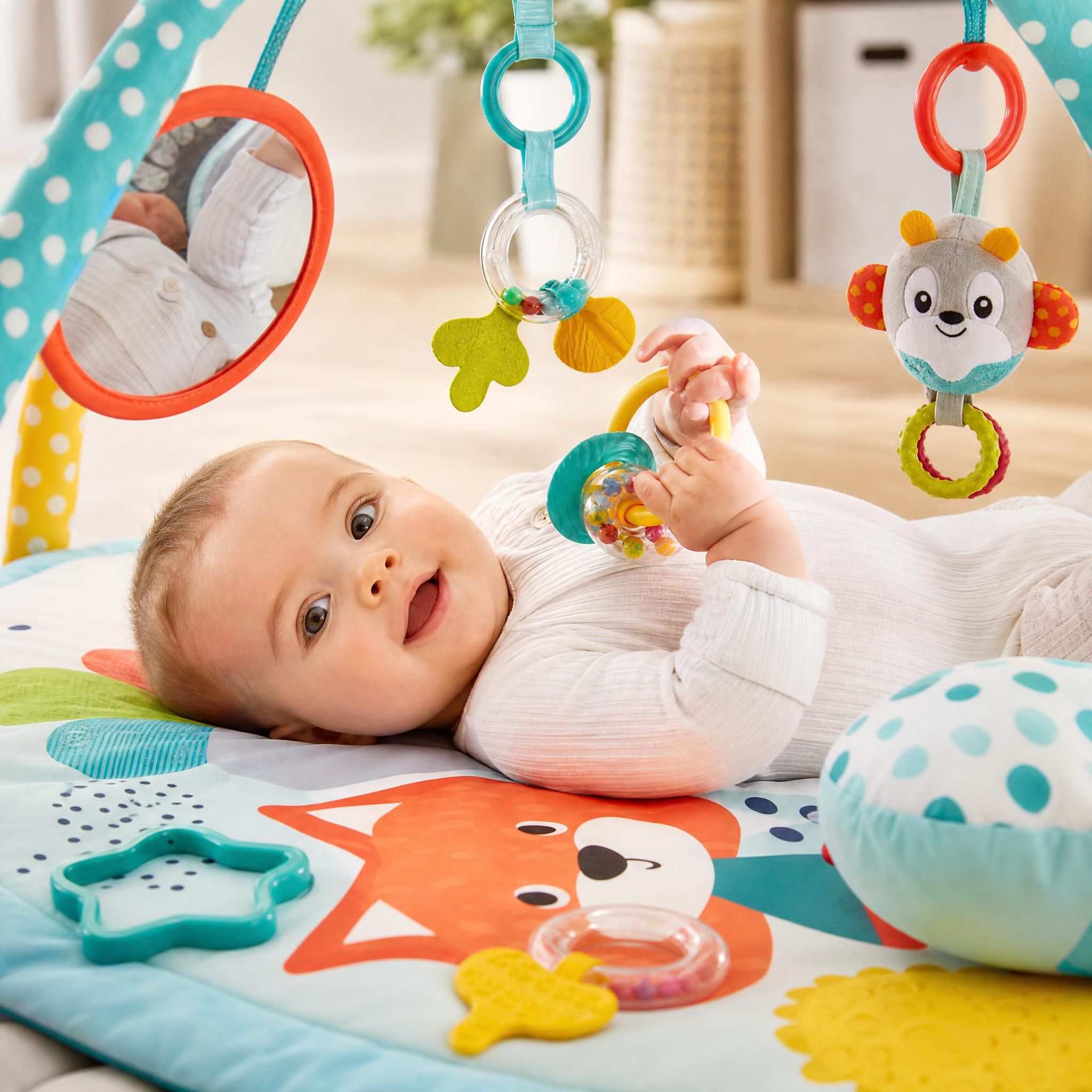 Bébé de 4 mois allongé sur un tapis d'éveil coloré avec des jouets sensoriels - hochets, miroir, anneaux de dentition