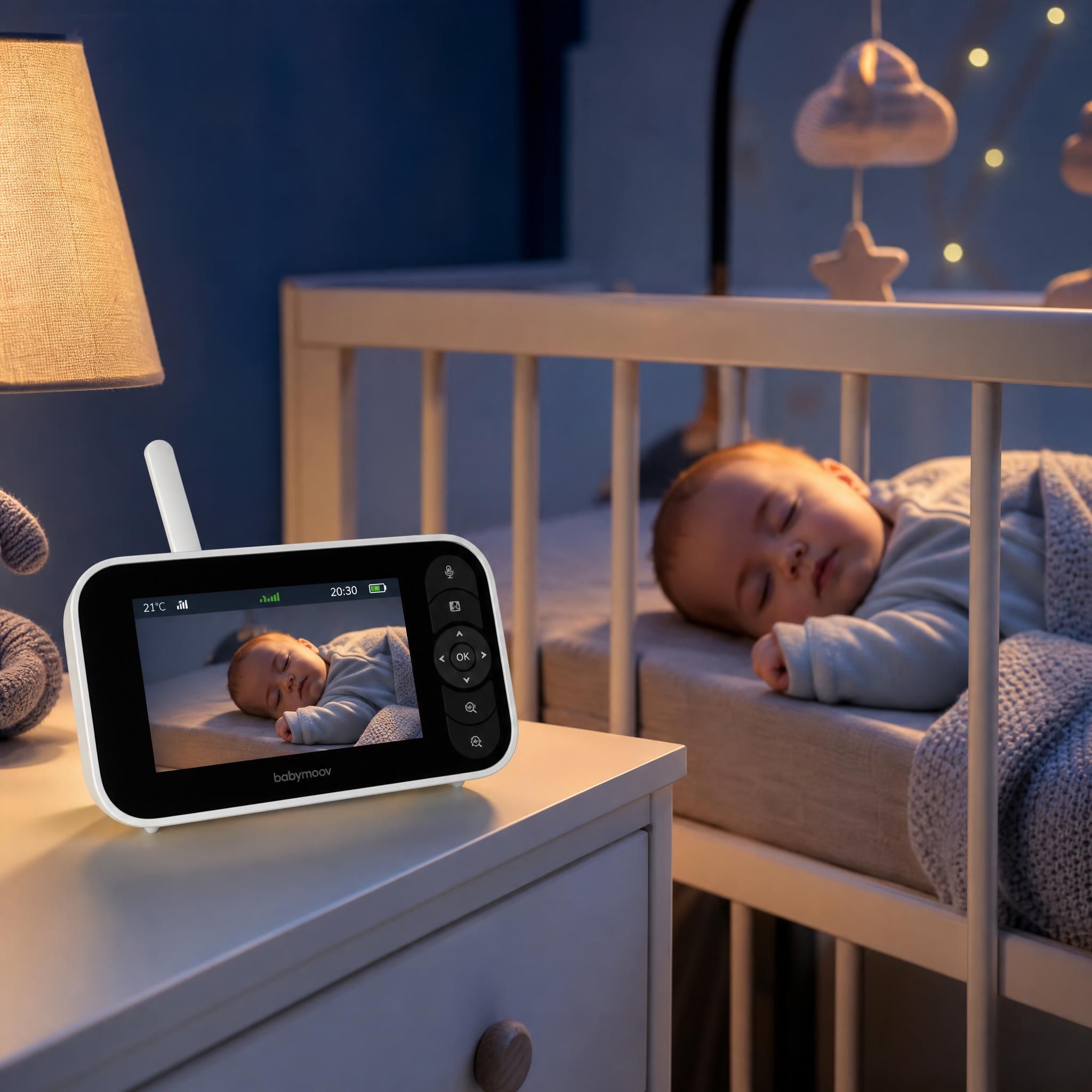 Babyphone vidéo connecté posé sur une table de nuit à côté d'un bébé endormi dans son berceau, ambiance douce nuit