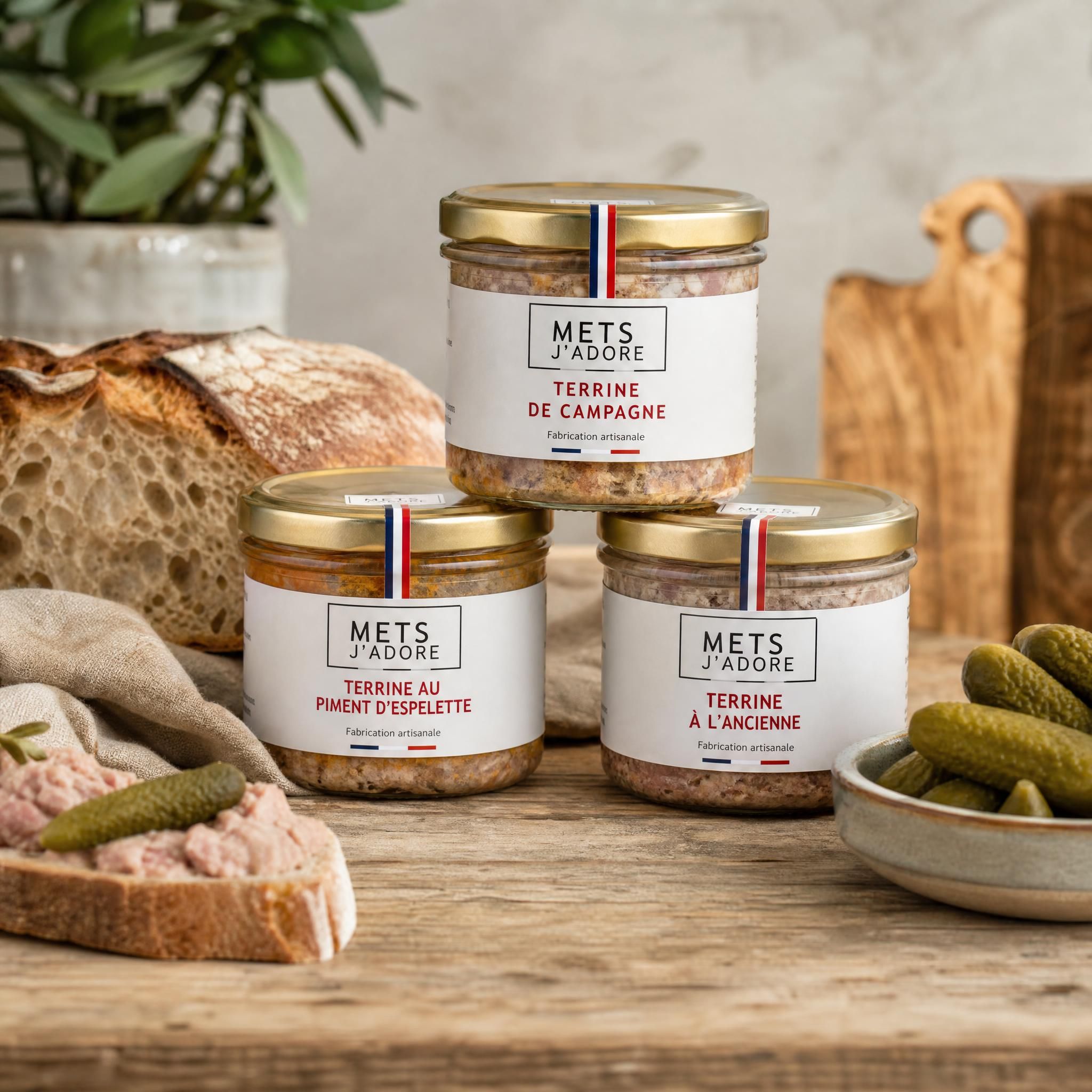 Bocaux de terrines artisanales Mets J'adore posés sur une table en bois rustique, avec du pain de campagne et des cornichons