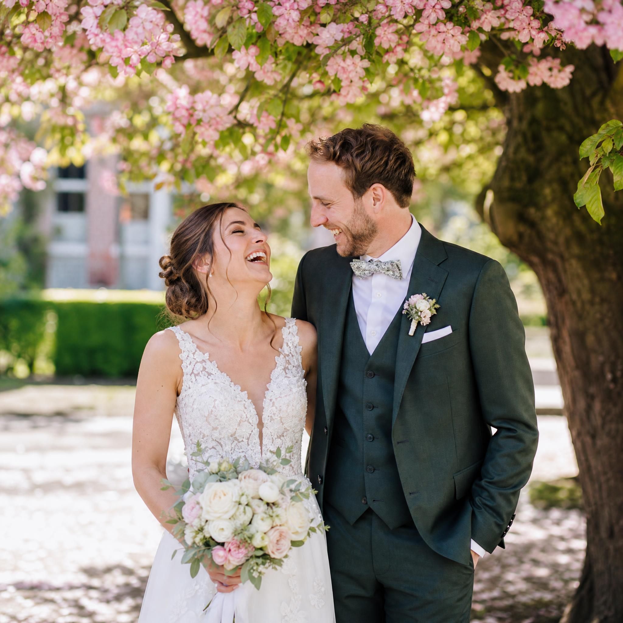 Couple de mariés riant sous un arbre en fleurs lors d'un reportage photo mariage naturel à Rixensart, Brabant wallon Belgique
