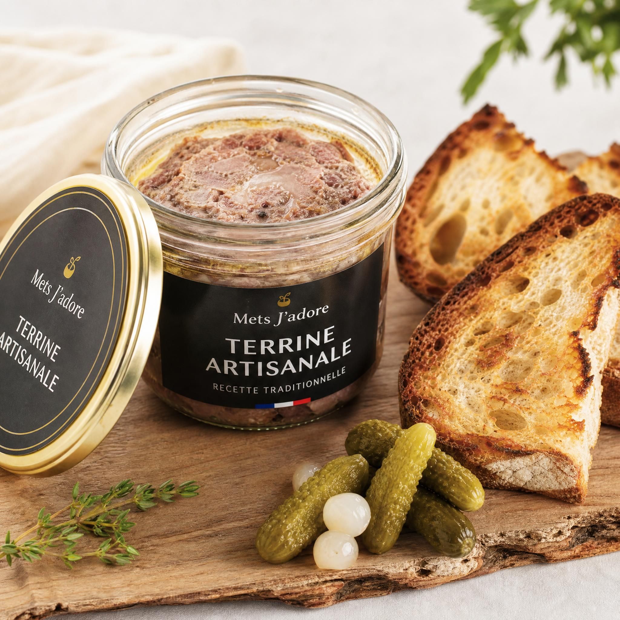 Terrine artisanale Mets J'adore ouverte sur une planche en bois avec des cornichons et du pain de campagne grillé