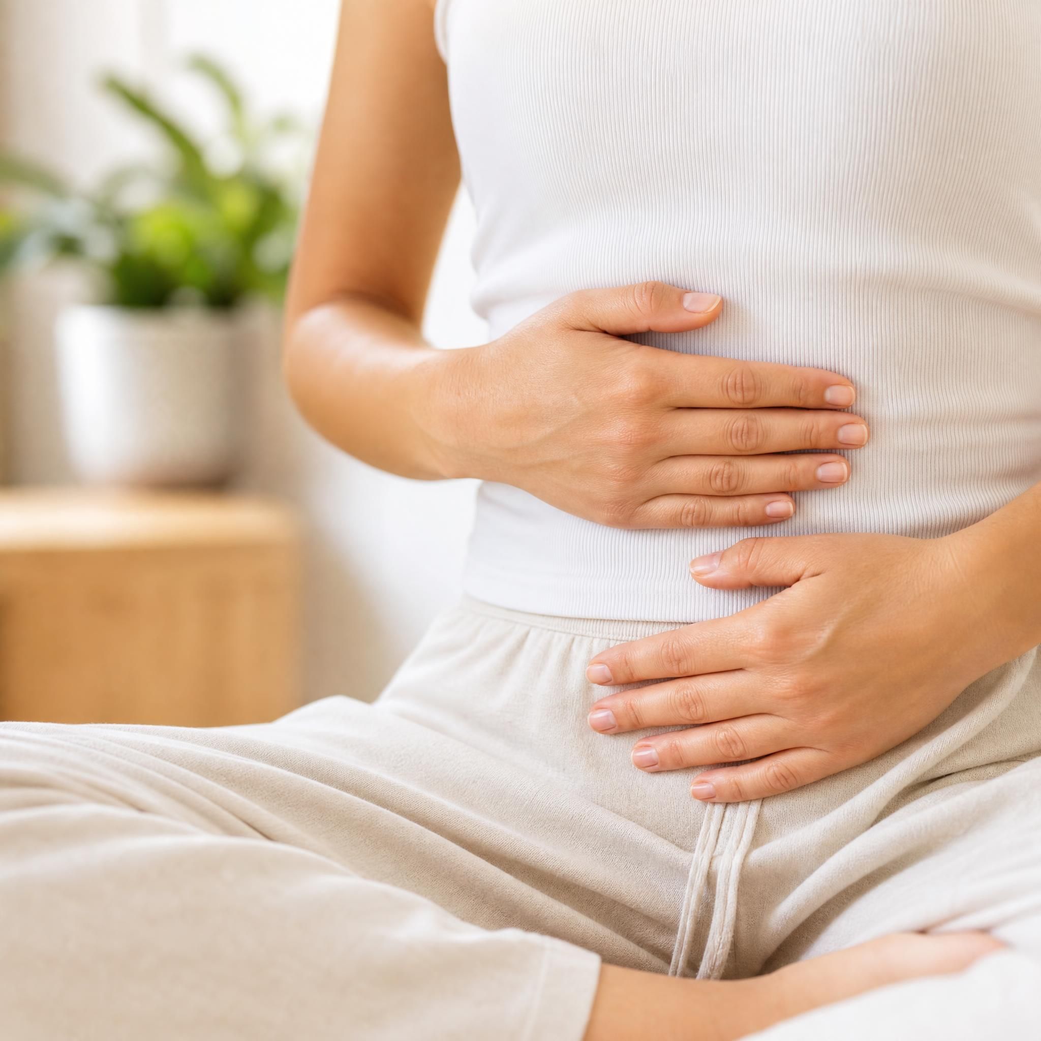 Gros plan sur des mains posées doucement sur le ventre d'une personne assise, en train de pratiquer la respiration abdominale dans un espace calme et lumineux