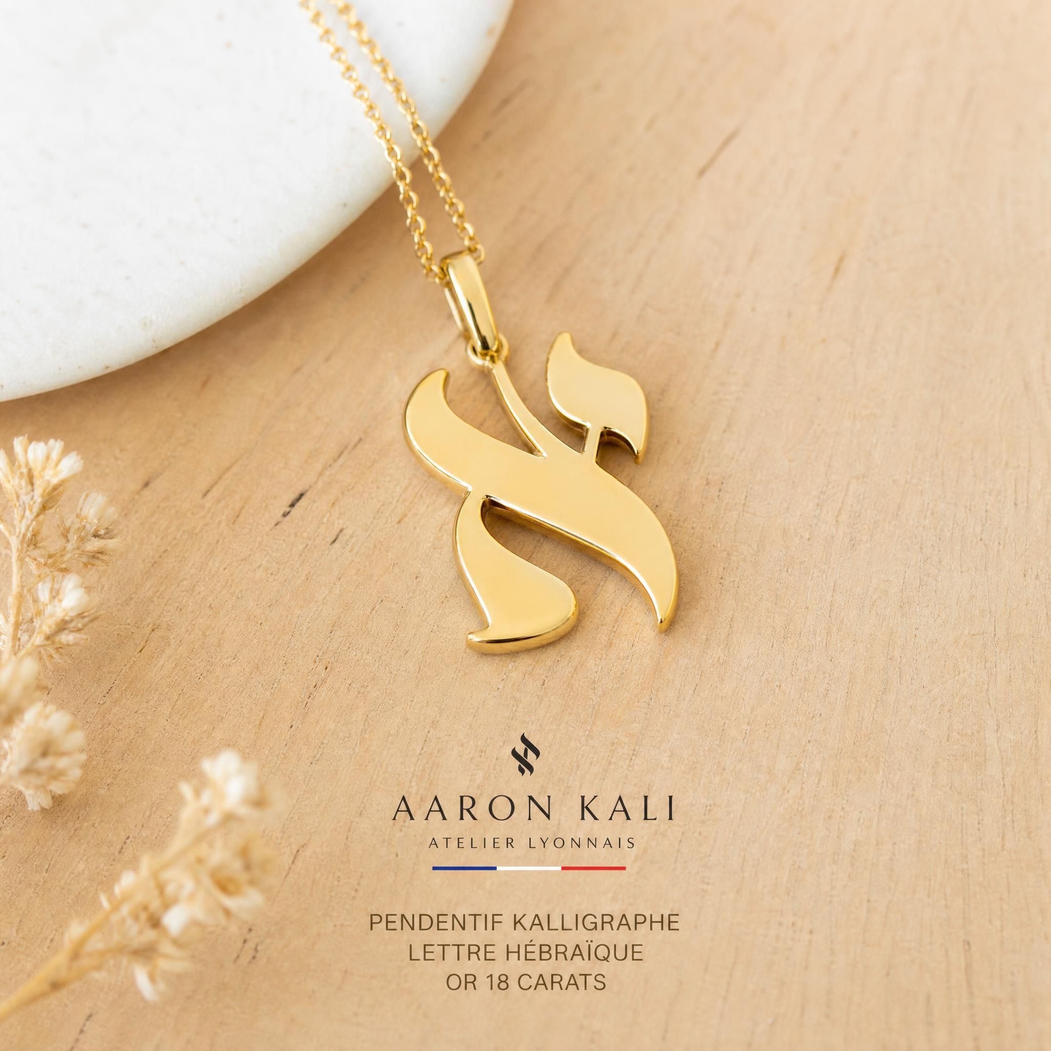 Pendentif Kalligraphe lettre hébraïque en or 18k jaune fabriqué à la main dans un atelier lyonnais, posé sur une surface en bois clair — bijou hébreu symbolique Aaron Kali