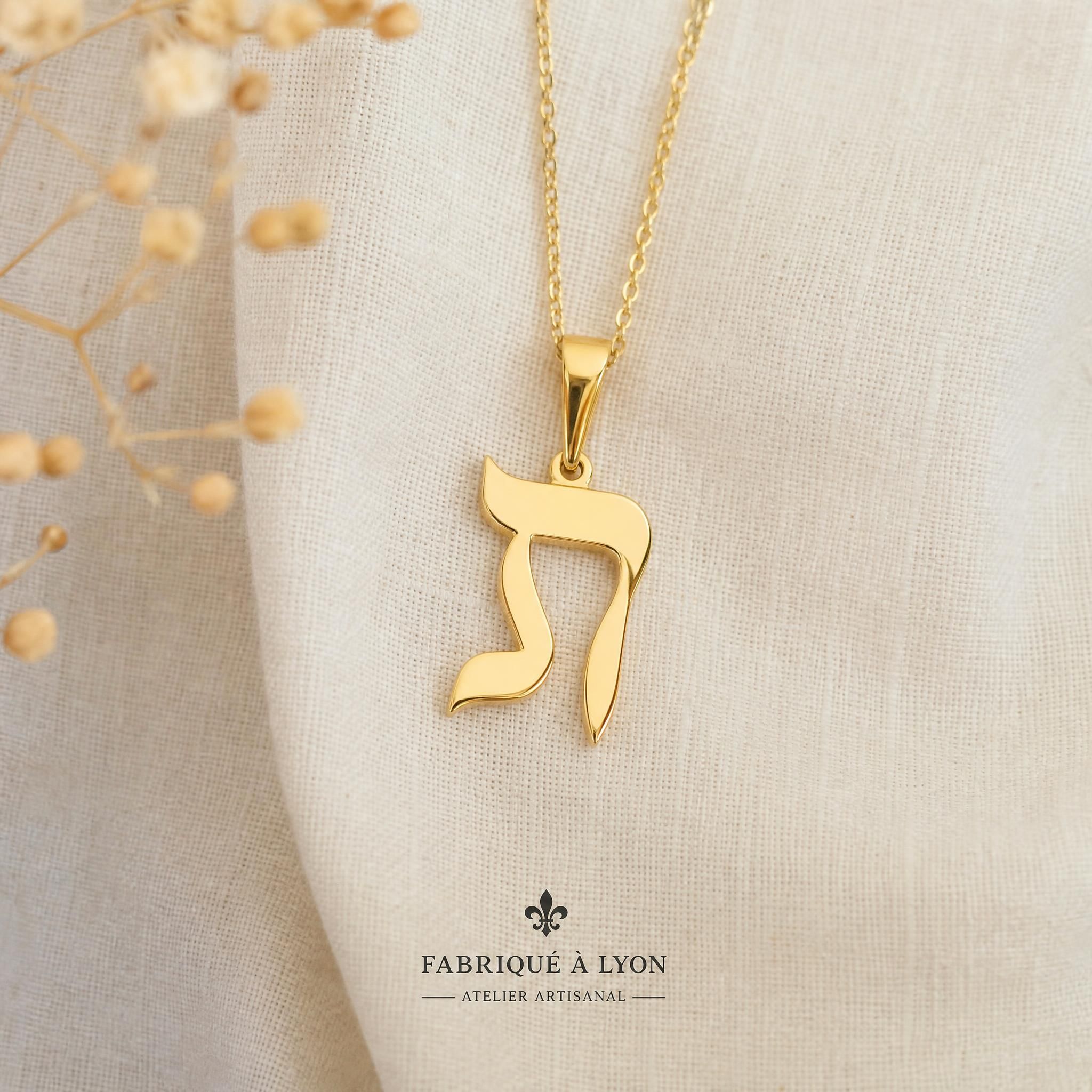 Pendentif lettre hébraïque Kalligraphe en or 18 carats jaune, fabriqué à la main dans un atelier lyonnais, posé sur fond de tissu naturel