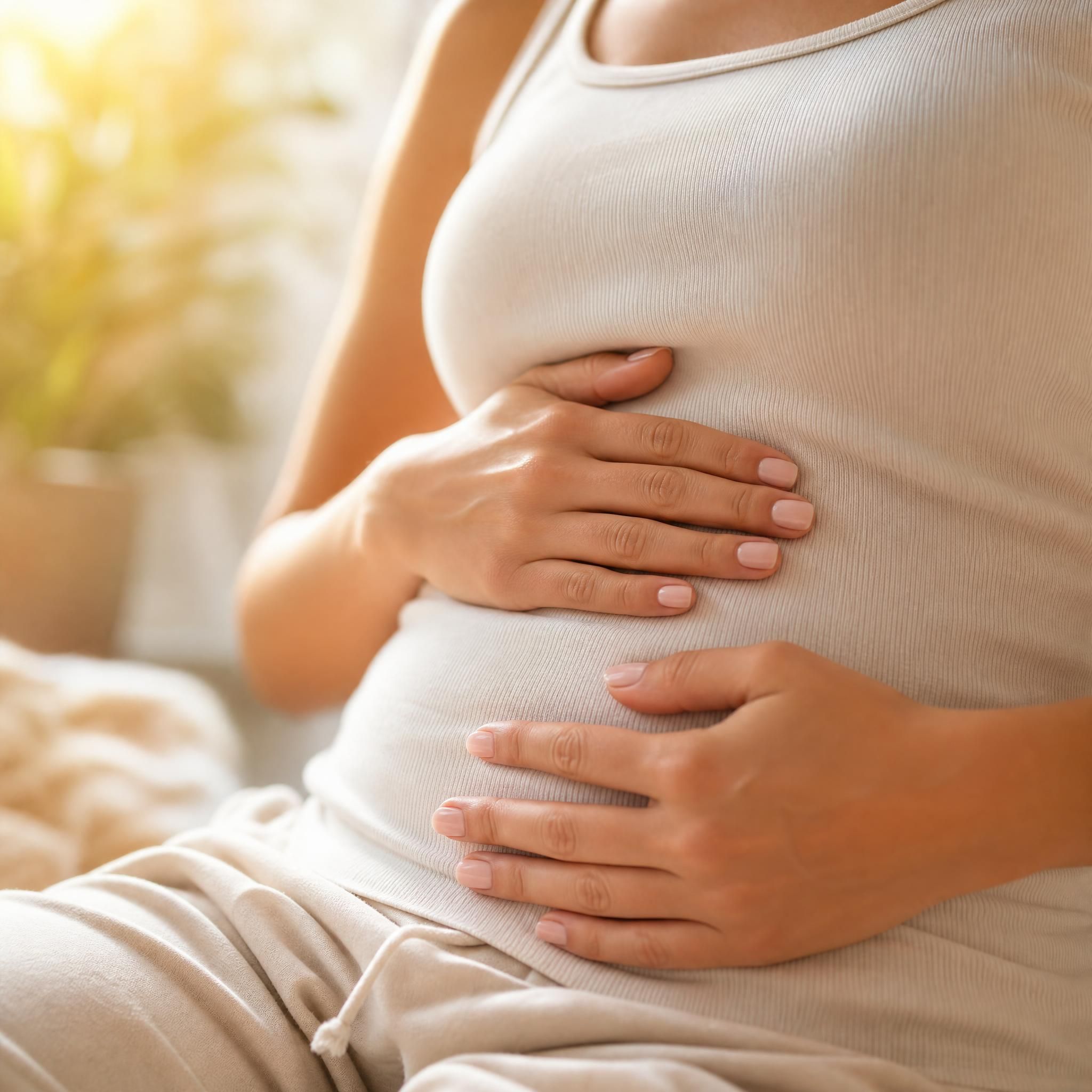 Gros plan sur les mains d'une femme posées sur son ventre, en train de pratiquer une respiration abdominale profonde, lumière naturelle dorée, ambiance calme et sécurisante