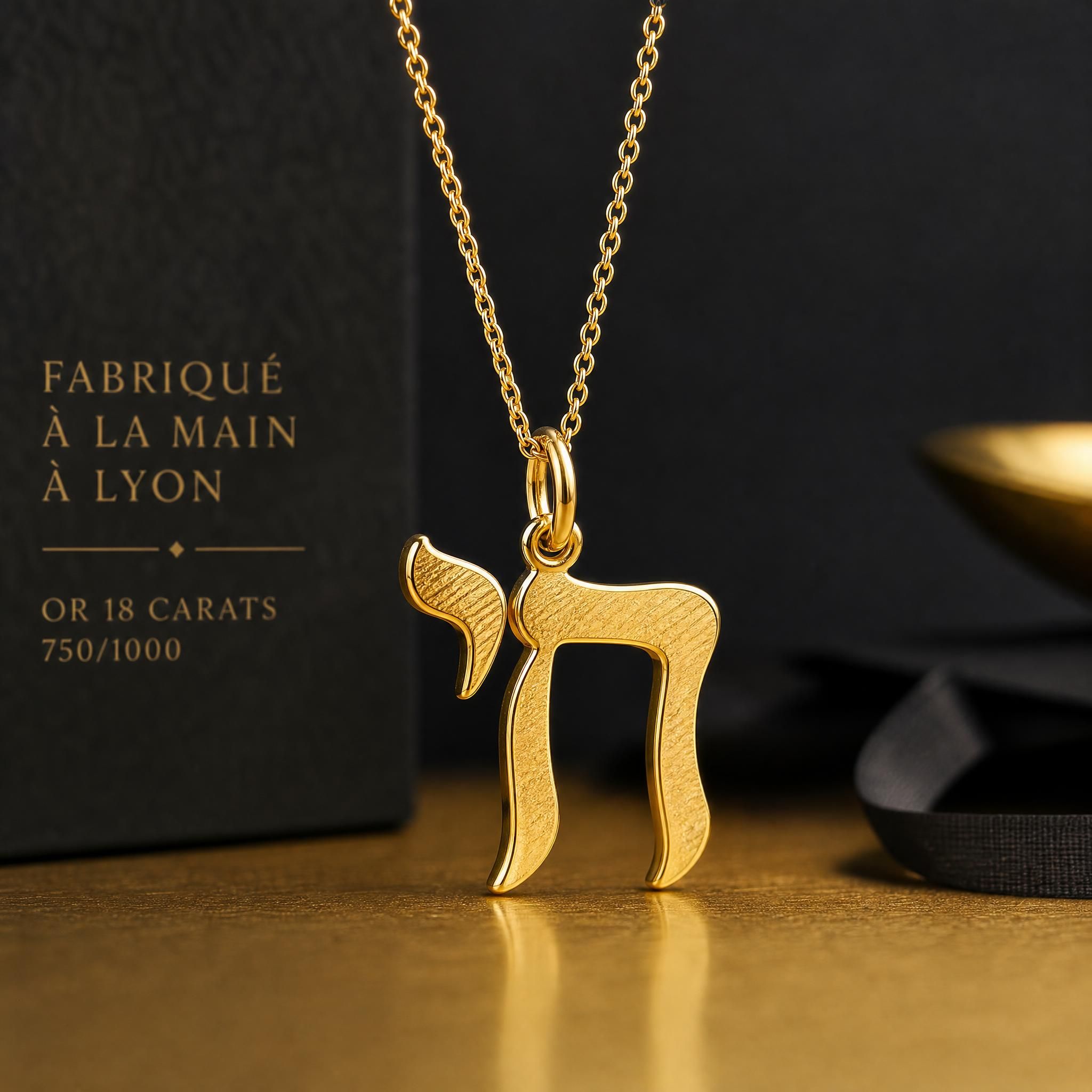 Pendentif lettre hébraïque Kalligraphe en or 18 carats jaune, fabriqué à la main dans un atelier lyonnais, posé sur une surface dorée avec un fond sombre et élégant