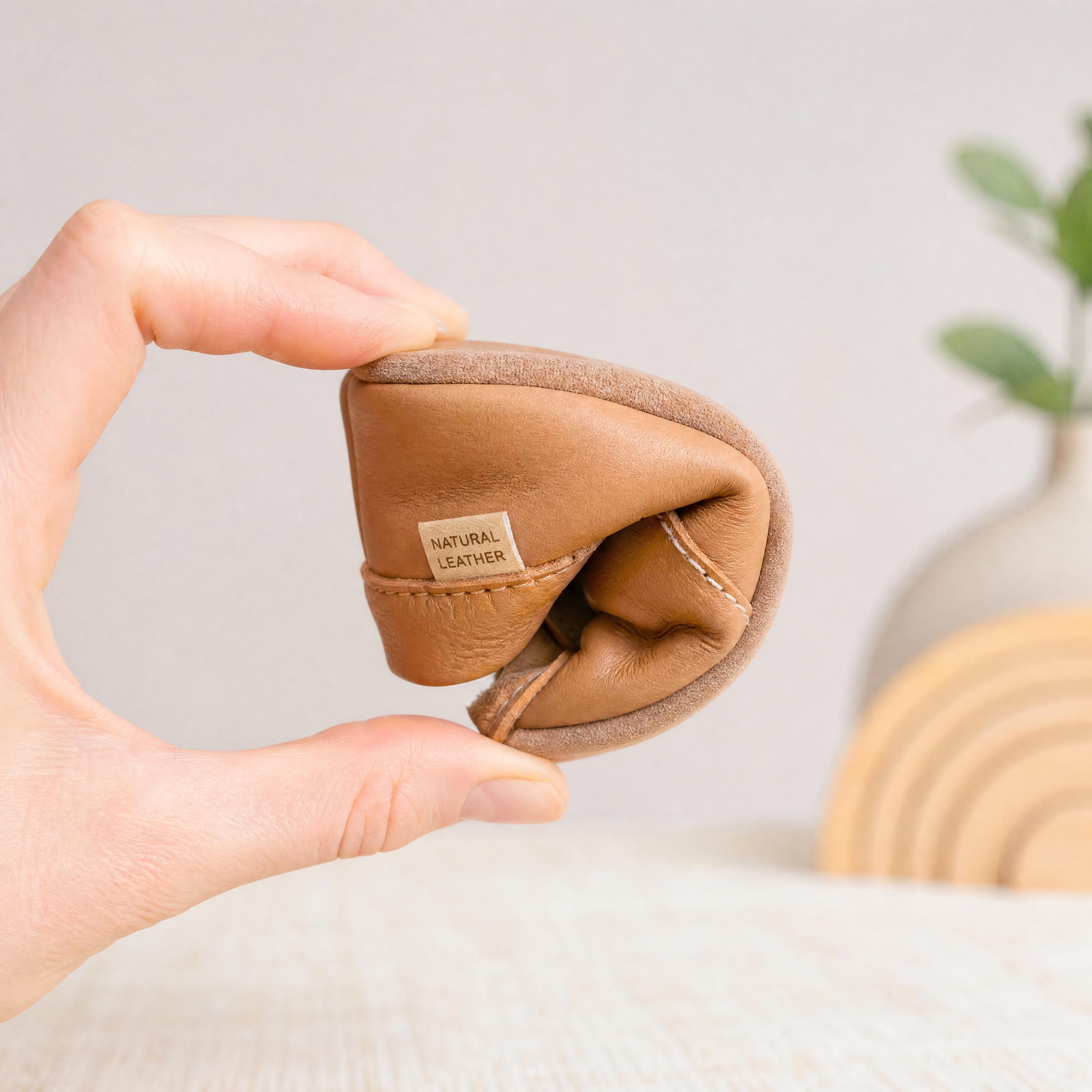Une paire de chaussures bébé souples en cuir naturel pliée facilement entre les doigts pour montrer sa flexibilité