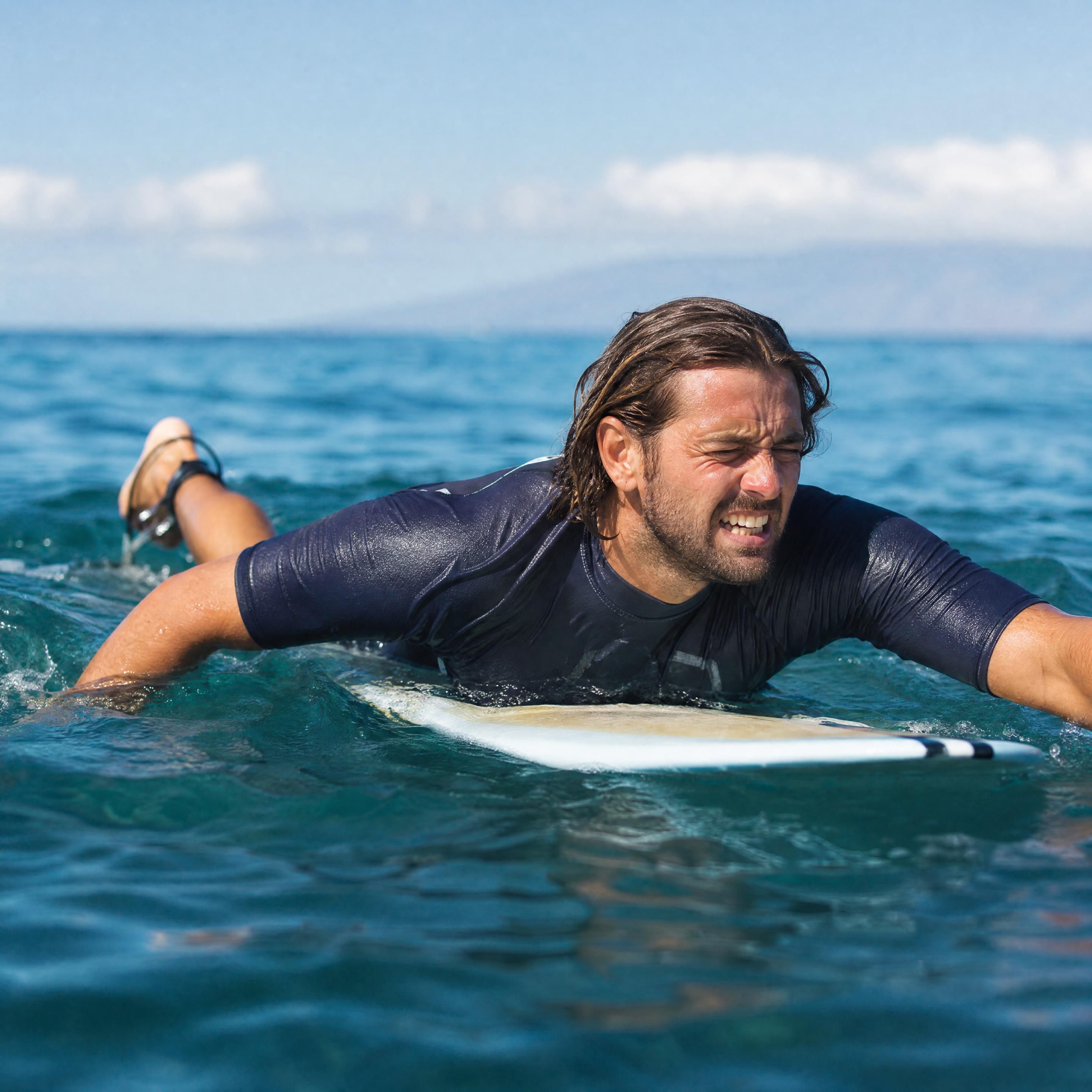 Surfeur débutant réalisant un échauffement des épaules et du dos sur la plage de Biarritz